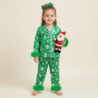 enfant vêtue d’un pyjama de noël vert sapin tenant une peluche du père noël