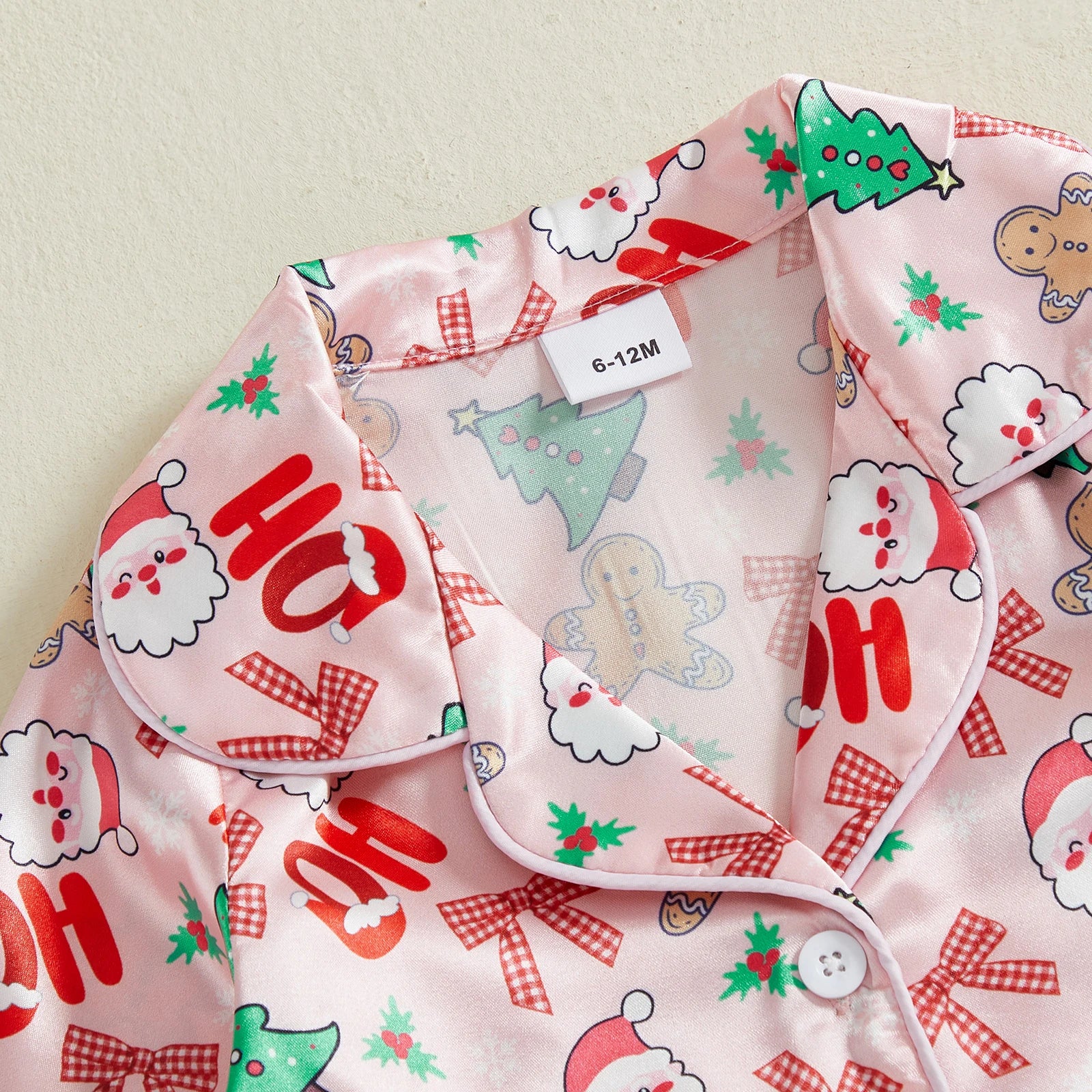 Détail du col d’un pyjama de Noël rose avec motifs Ho Ho Ho, sapins et bonhommes pain d’épices