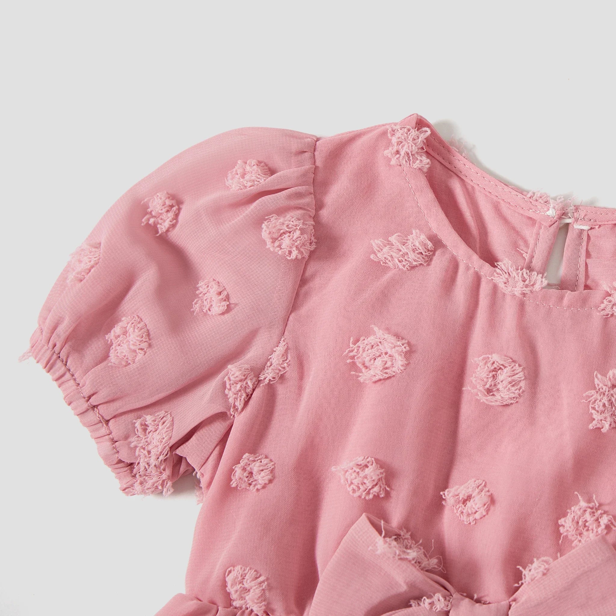 Détail du tissu à pois en relief et des manches bouffantes de la robe rose