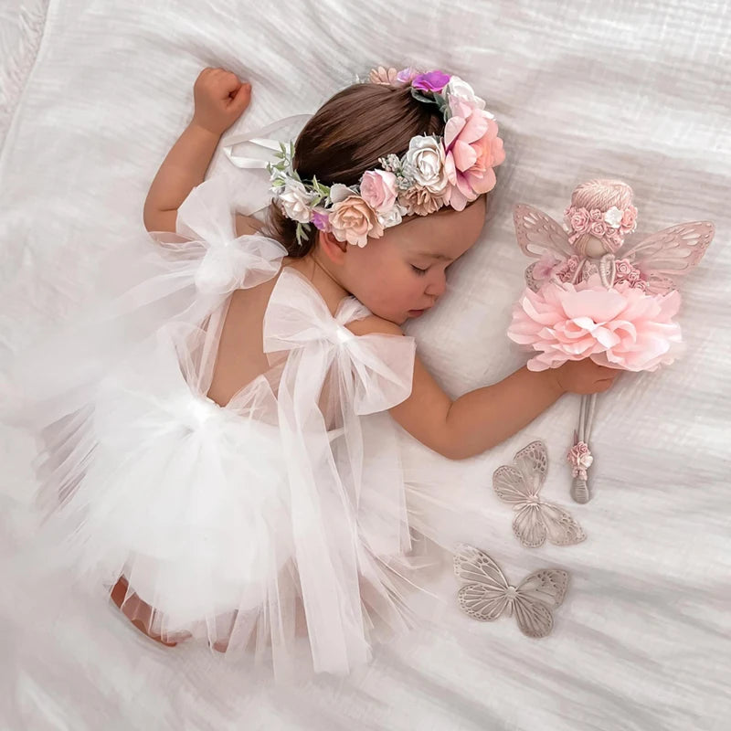 Bébé endormi avec couronne de fleurs et portant une tenue de baptême blanche