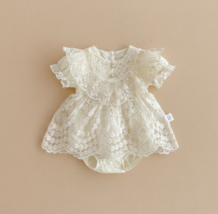 Barboteuse de cérémonie pour bébé couleur ivoire avec bustier en dentelle florale, boutons perles et manches bouffantes festonnées