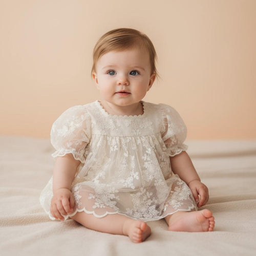 Bébé fille portant la barboteuse de cérémonie Milana beige avec superposition en dentelle florale