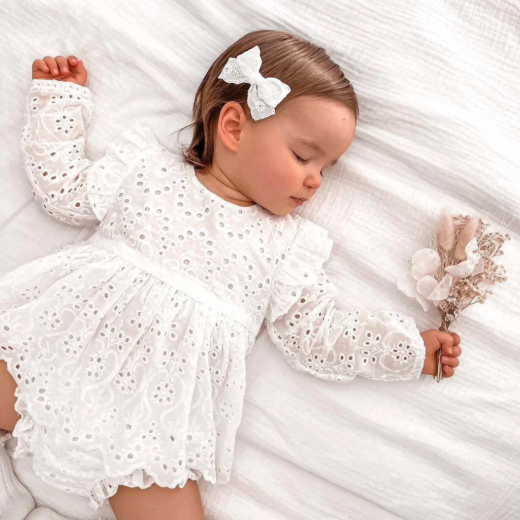 Bébé allongé portant la robe de baptême blanche avec ses détails fleuris et son short