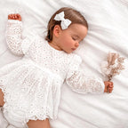 Bébé allongé portant la robe de baptême blanche avec ses détails fleuris et son short