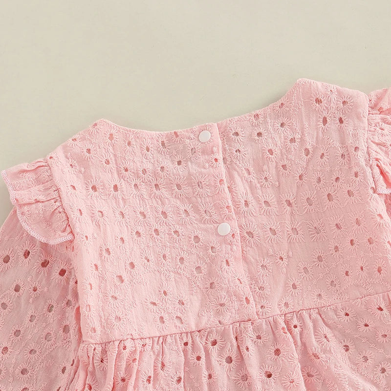 Détail de la bordure en dentelle ajourée sur une robe de baptême rose