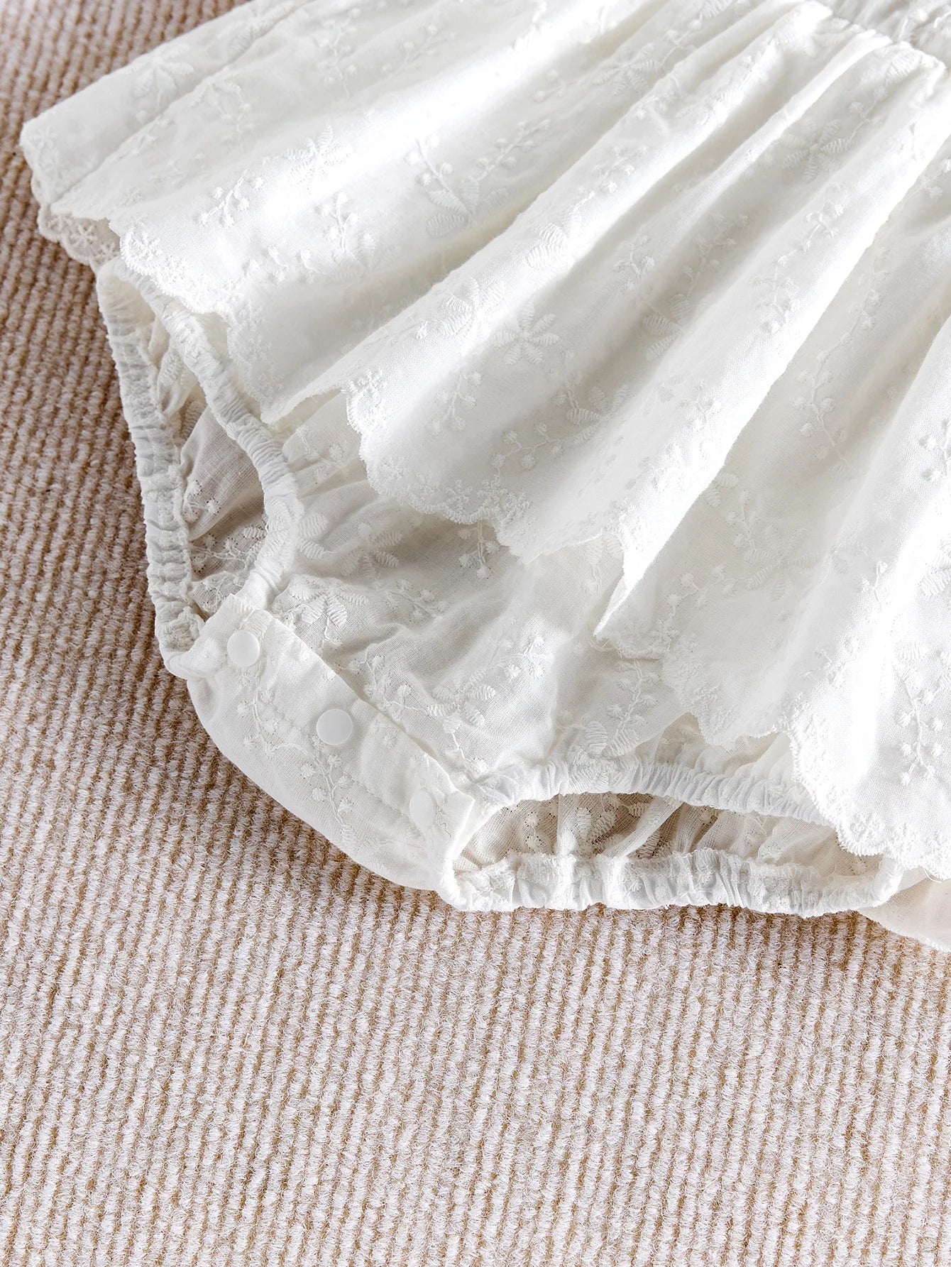Détail des broderies délicates sur le bas d'une barboteuse de baptême blanche.