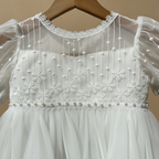 Zoom sur les perles nacrées et la dentelle travaillée du bustier d'une robe de baptême