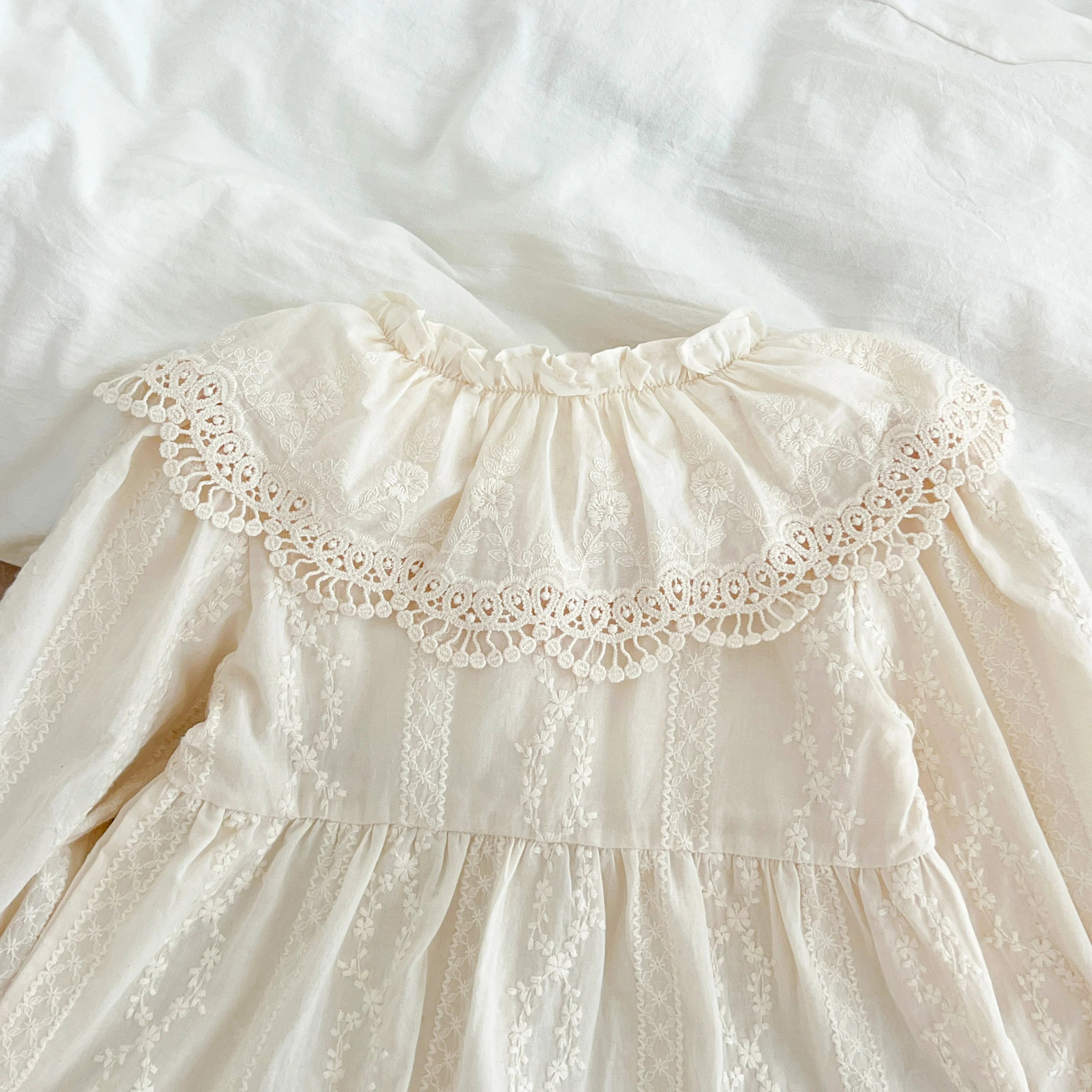 Détail du col claudine à volants avec broderie anglaise raffinée sur coton beige
