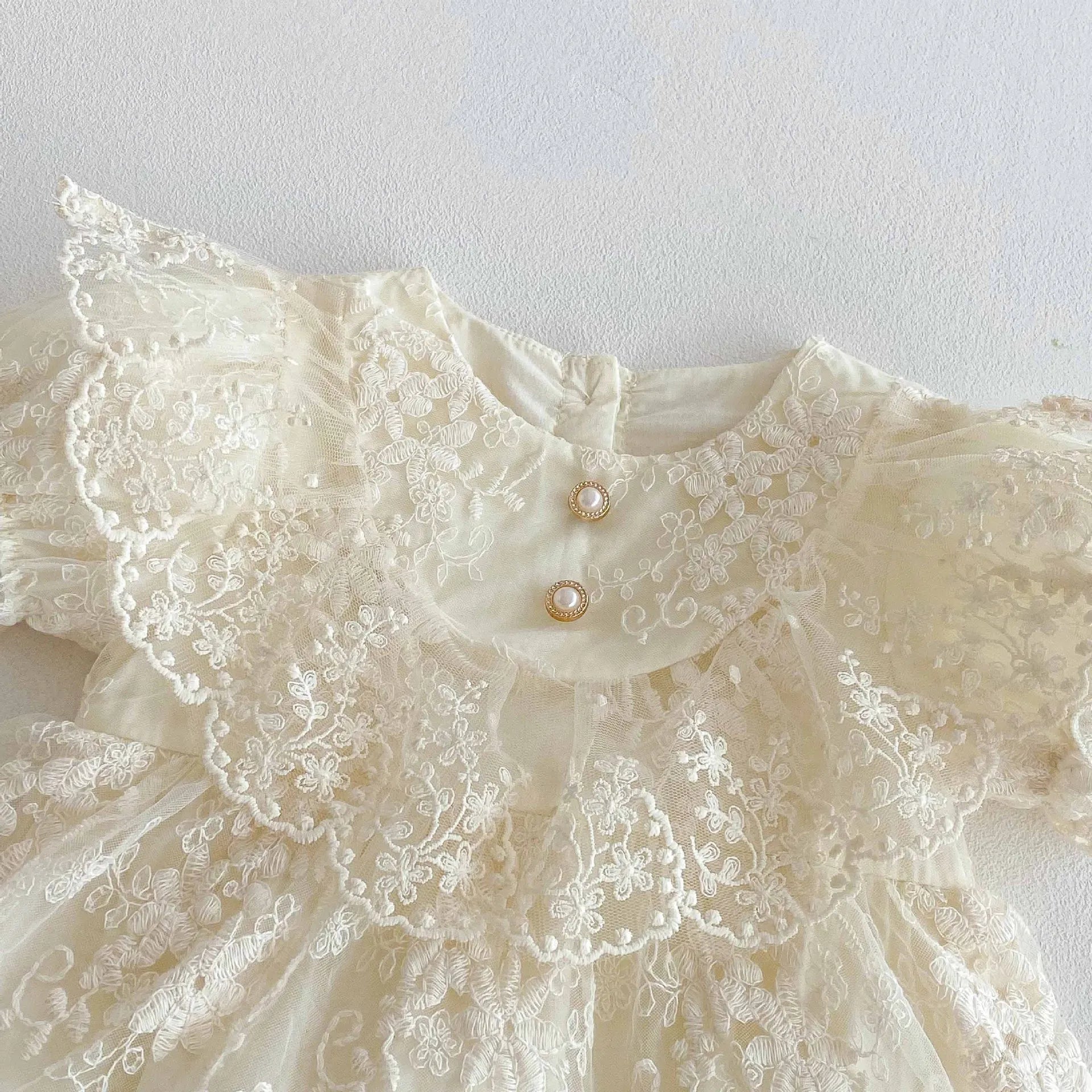 Détail de la manche bouffante festonnée et du col rond en dentelle de la barboteuse de fête Juliette