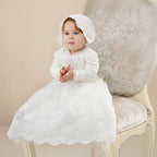 Bébé portant la robe de baptême longue Angélique avec son bonnet assorti sur un fauteuil classique