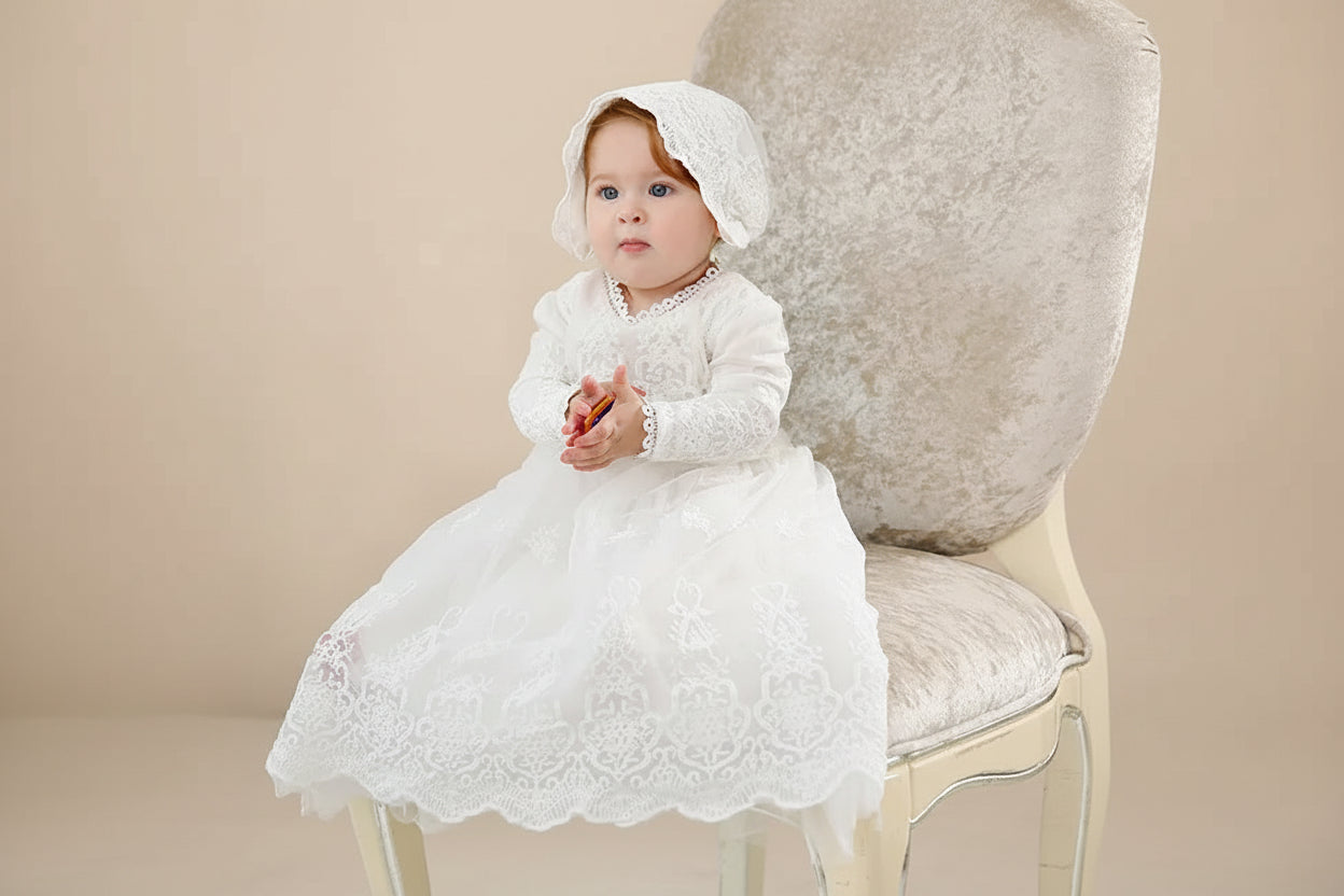 Bébé portant la robe de baptême longue Angélique avec son bonnet assorti sur un fauteuil classique