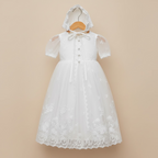 Robe de baptême blanche à manches courtes présentée sur cintre avec son bonnet de cérémonie assorti