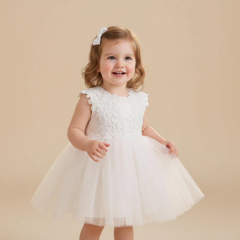 Petite fille souriante portant une robe de baptême blanche avec motifs fleurs marguerites sur le bustier
