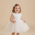 Petite fille souriante portant une robe de baptême blanche avec motifs fleurs marguerites sur le bustier