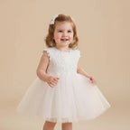 Petite fille souriante portant une robe de baptême blanche avec motifs fleurs marguerites sur le bustier