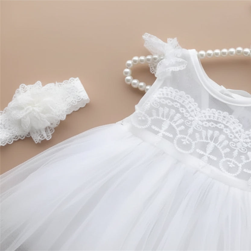 Robe de cérémonie blanche pour bébé présentée sur un cintre avec son bandeau à fleurs