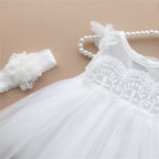 Robe de cérémonie blanche pour bébé présentée sur un cintre avec son bandeau à fleurs