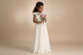 Petite fille portant une robe de cérémonie bohème longue blanche avec bouquet de fleurs.