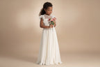 Petite fille portant une robe de cérémonie bohème longue blanche avec bouquet de fleurs.