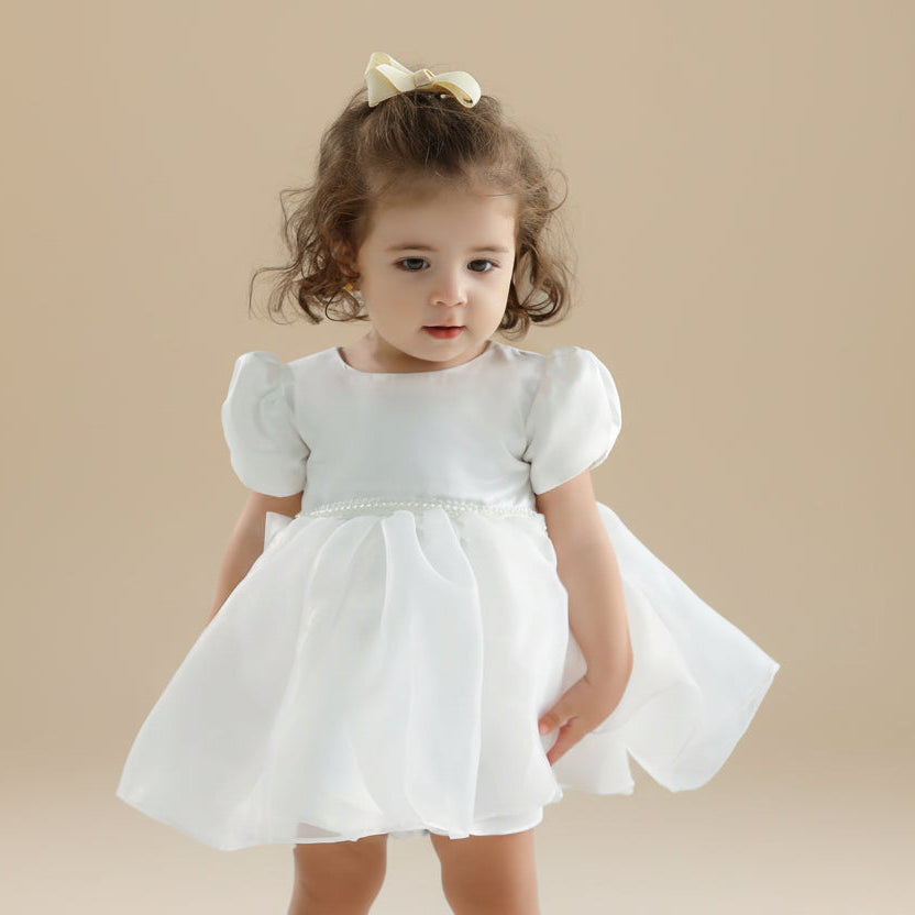 Portrait de face d'une petite fille en robe de demoiselle d'honneur blanche avec ceinture perlée