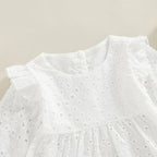 Détail des motifs ajourés et de la dentelle sur le bustier d'une robe de baptême blanche
