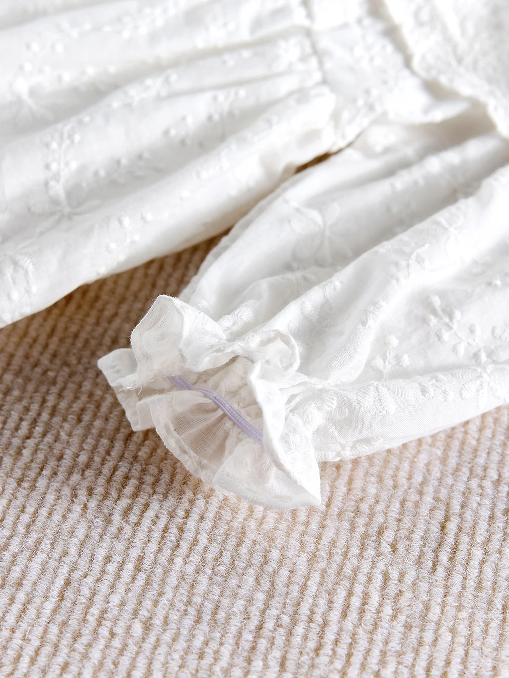 Zoom sur le tissu en coton et les finitions élastiquées de la barboteuse bébé.