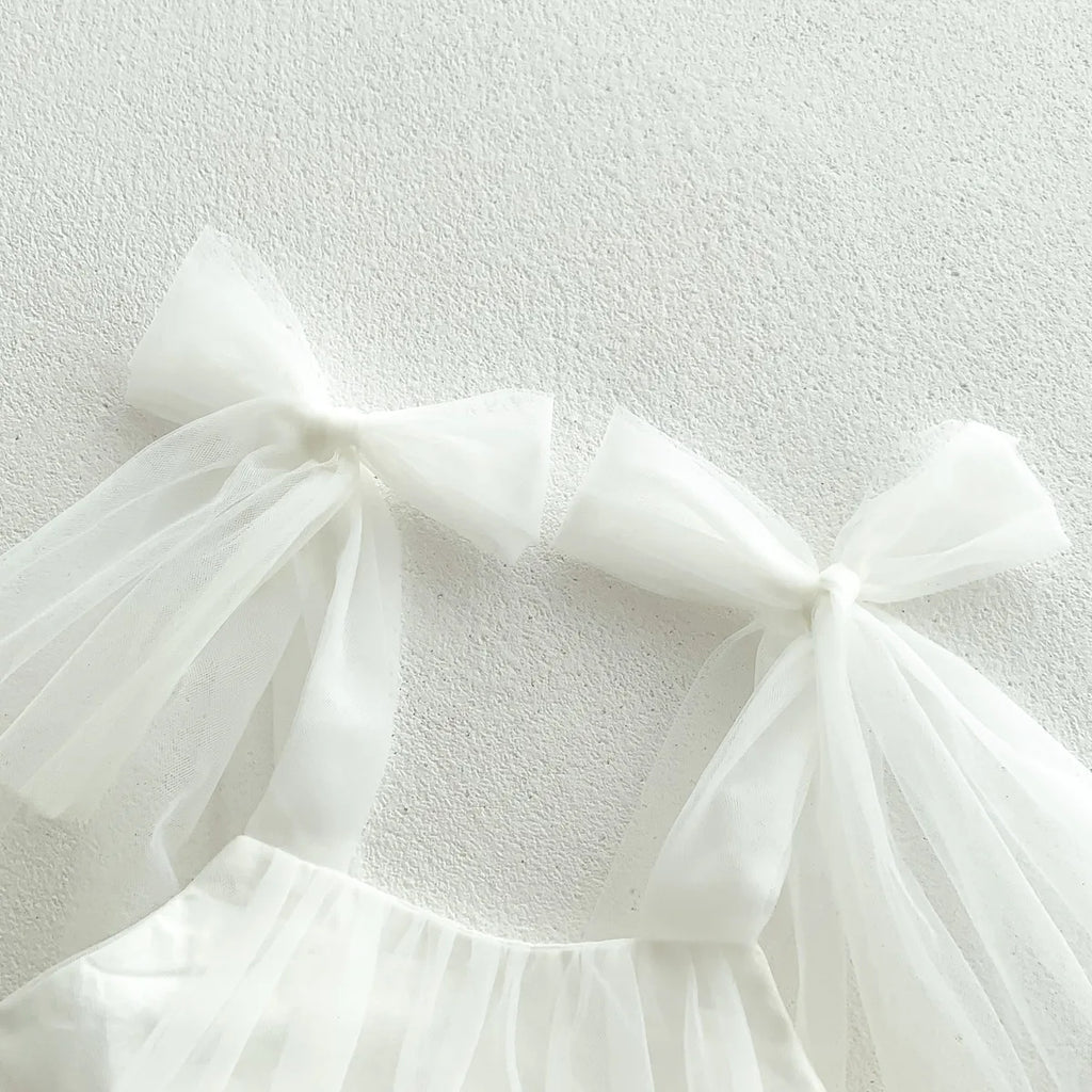 Gros plan sur le détail du nœud en tulle transparent sur l'épaule de la barboteuse blanche